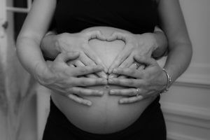 Ventre de femme enceinte avec des mains formant un coeur