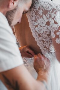 Préparatifs : le marié aide la mariée pour la robe